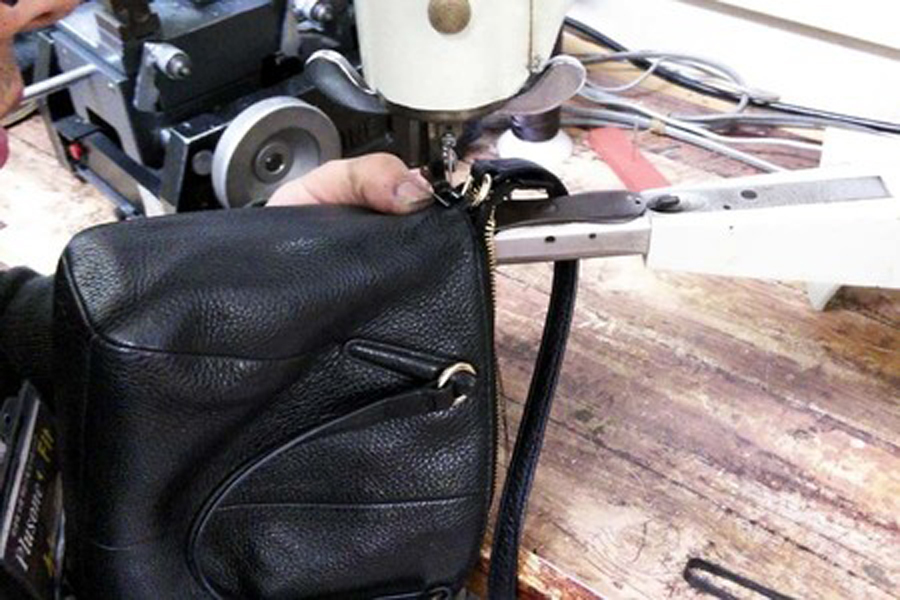 カバン修理例としてコーチ （COACH）のバッグ、ショルダーベルトの付け根部分を入れ込んだ箇所を八方ミシン（皮革製品専用ミシン）で縫い込んでる様子